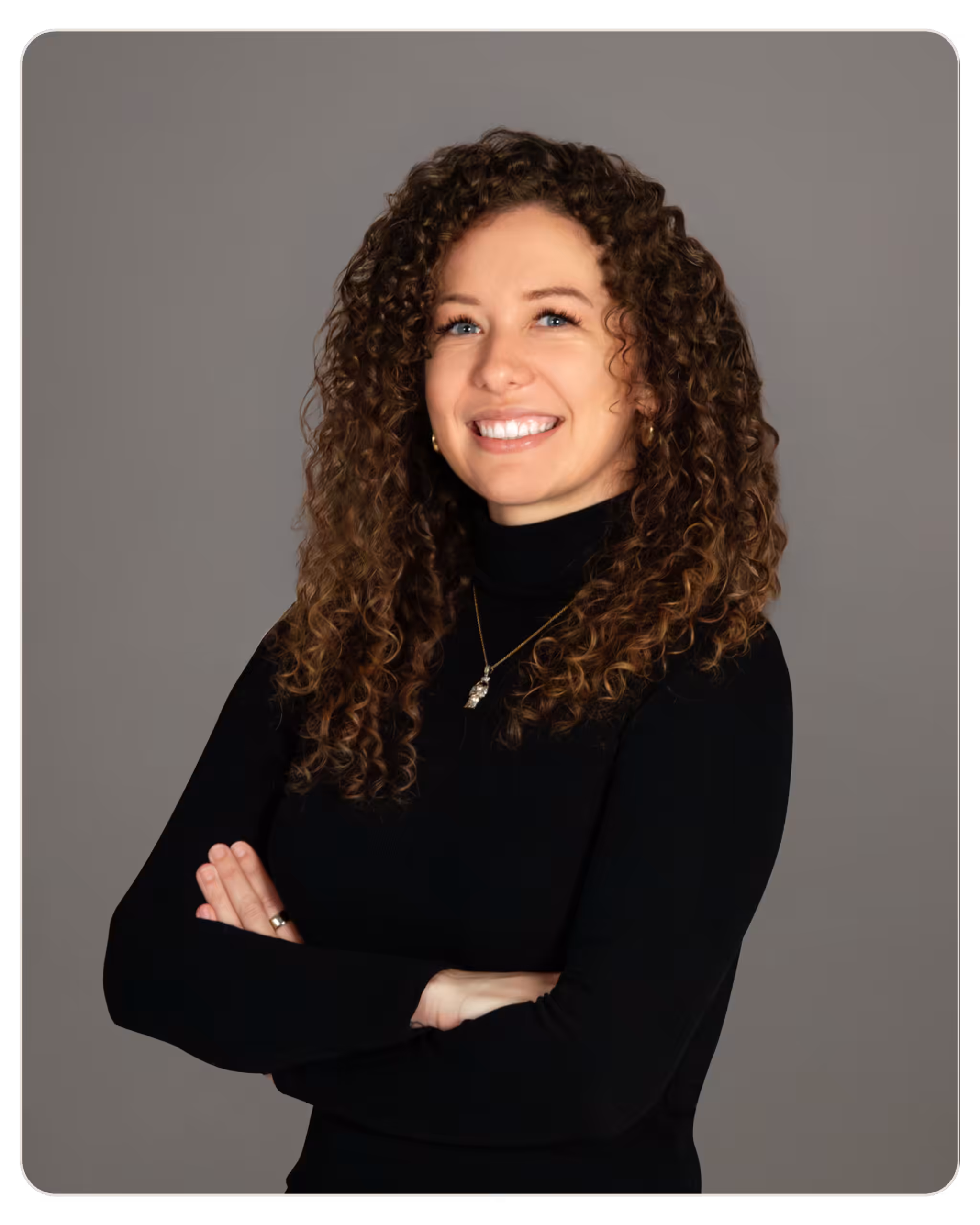 beacon Alyse Mitchell, MSW, RCSWI Smiling woman with curly hair and crossed arms wearing a black turtleneck, posing against a gray backdrop.
