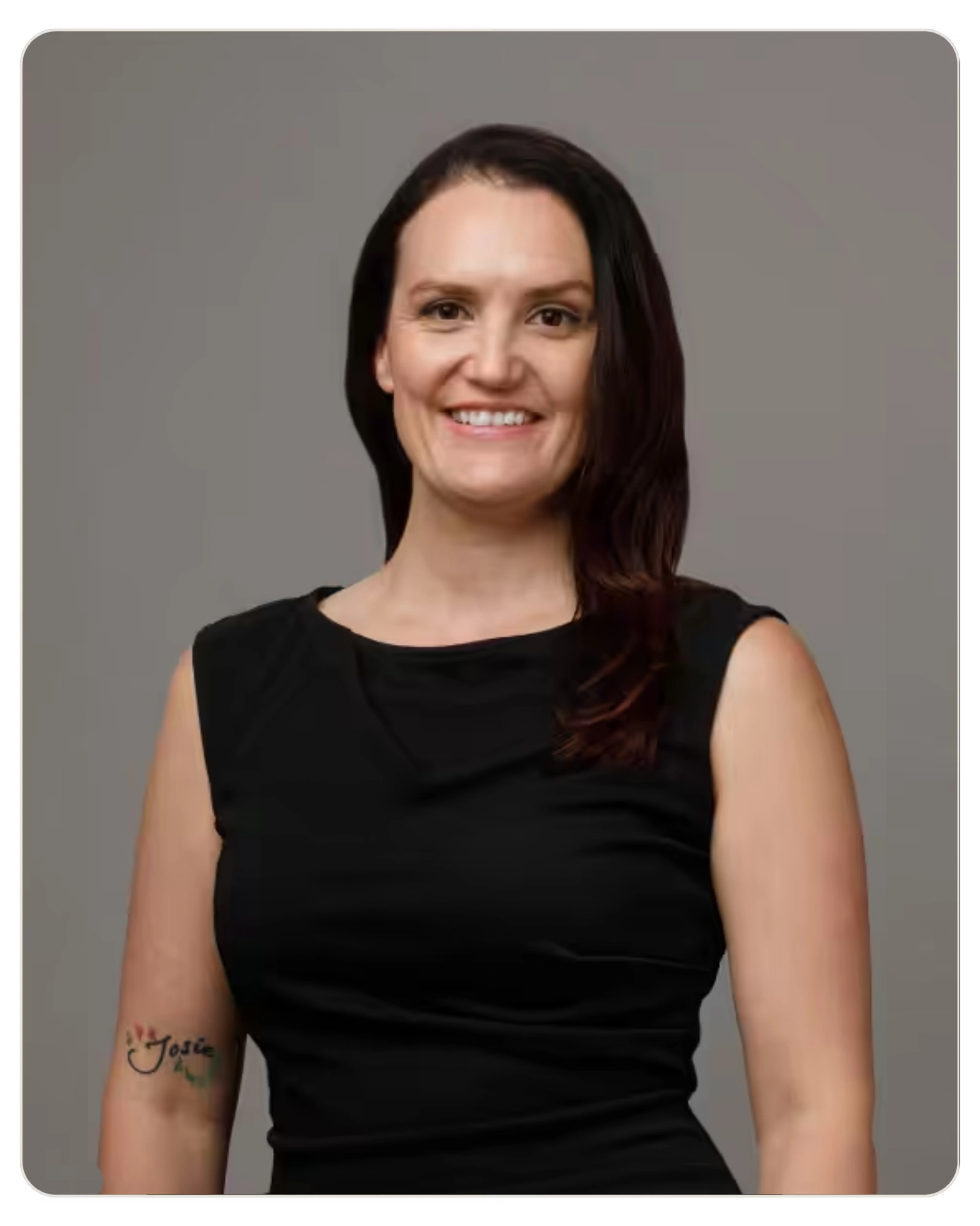 Smiling woman in a black sleeveless top posing against a gray studio backdrop, dark hair framing her face.