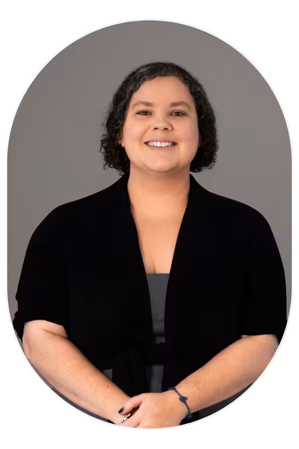 Smiling woman with short curly hair wearing a black cardigan against a gray background (portrait).