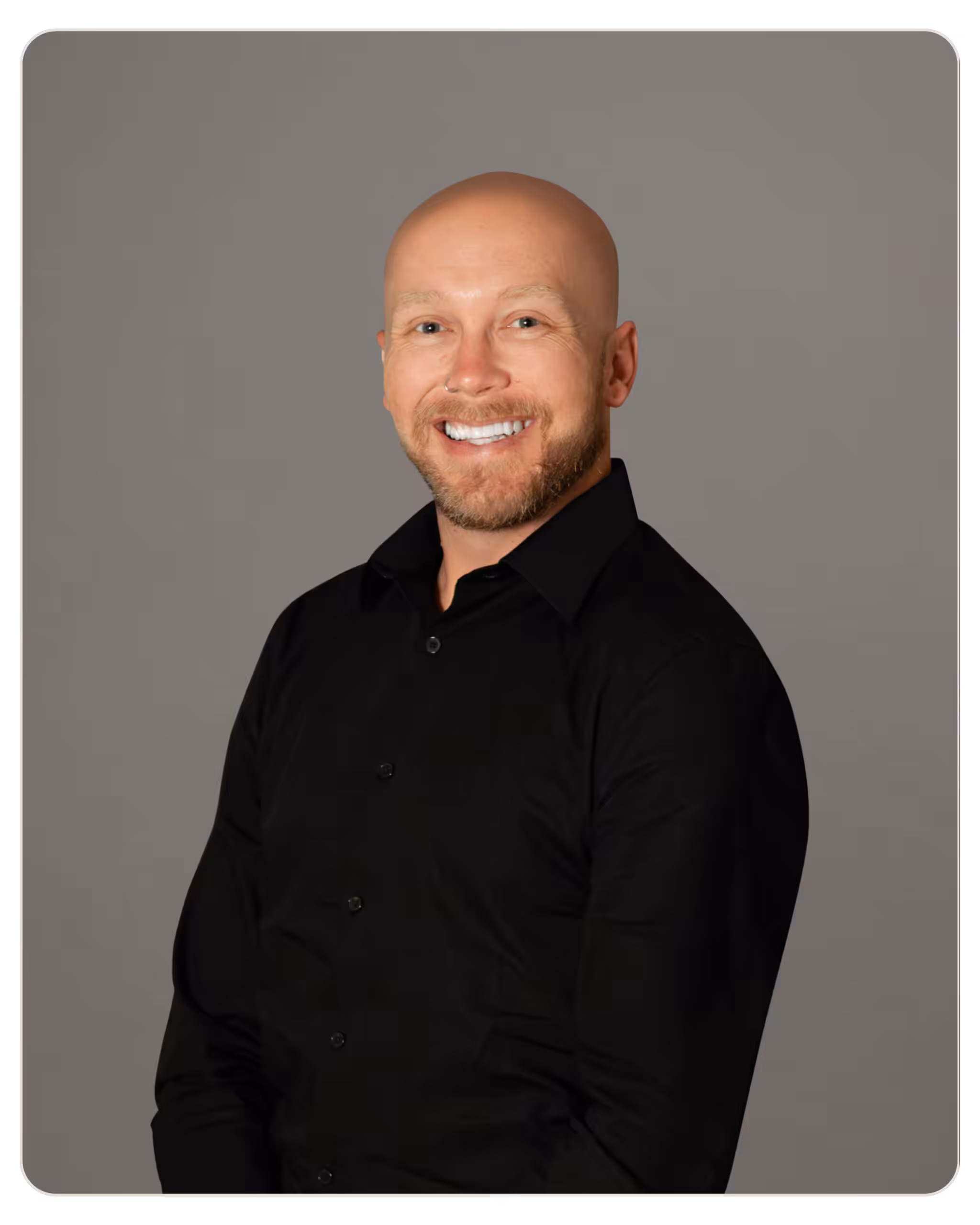 Beacon- Colt Crowser, CAC, ICADC Smiling bald man with a short beard wearing a black shirt against a gray studio background.