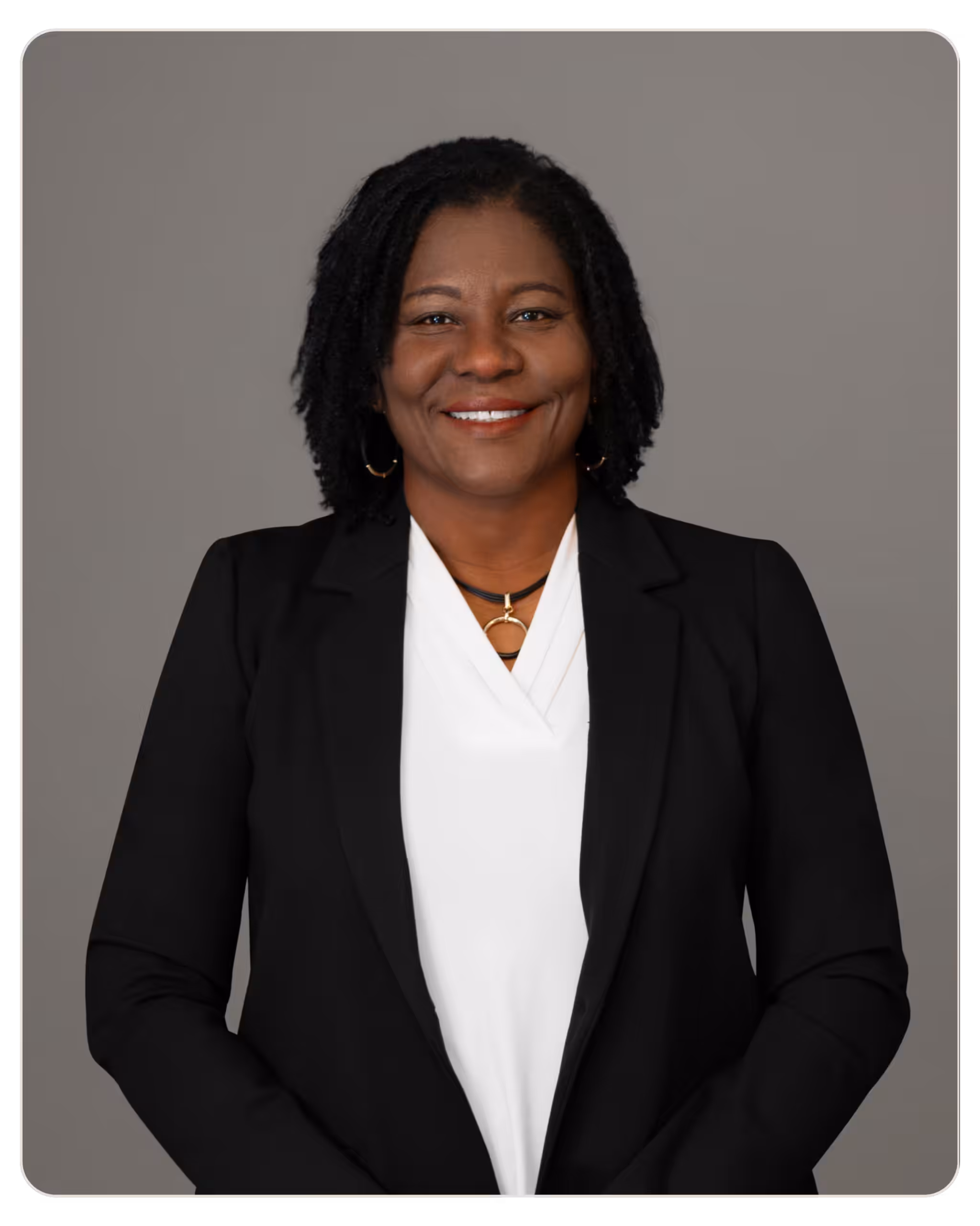 Marie Eliacin, RN BSN: Director of Nursing at Beacon. Smiling Black woman in a black blazer and white blouse, posed for a professional headshot against a gray background.