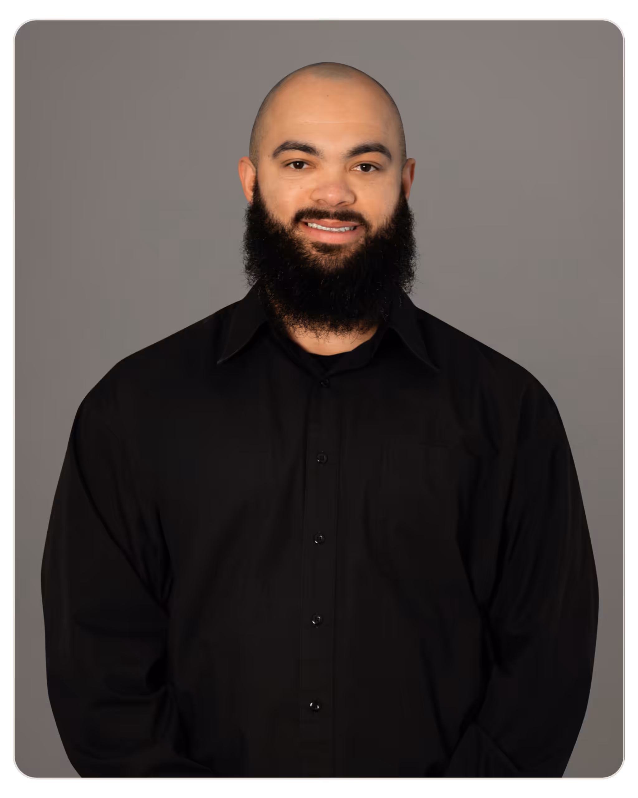 Beacon - Michael Kennedy Head-and-shoulders portrait of a smiling man with a full beard and shaved head in a black button-up shirt against a gray studio backdrop.