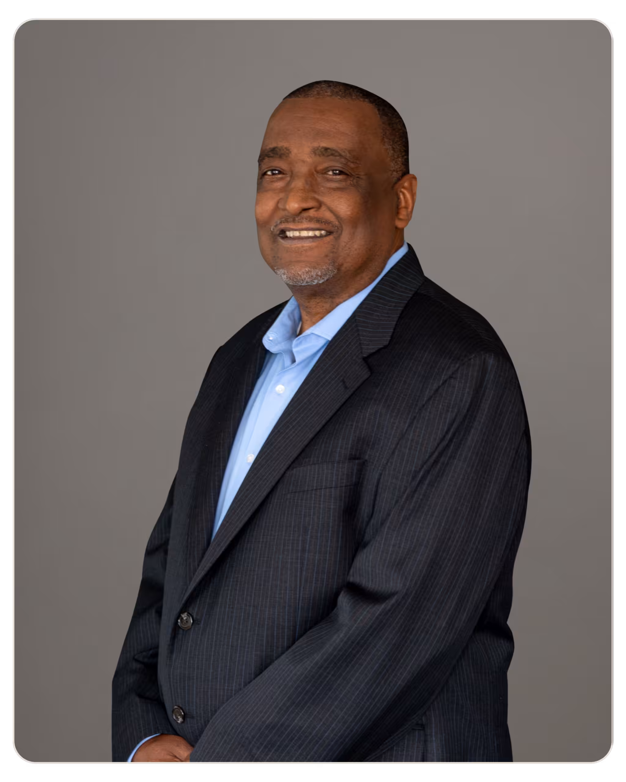 Paul Stephens, MS APCC: Recovery Coach at Radar. Smiling man in a dark pinstripe suit and light blue shirt, posing for a formal portrait with a gray backdrop.
