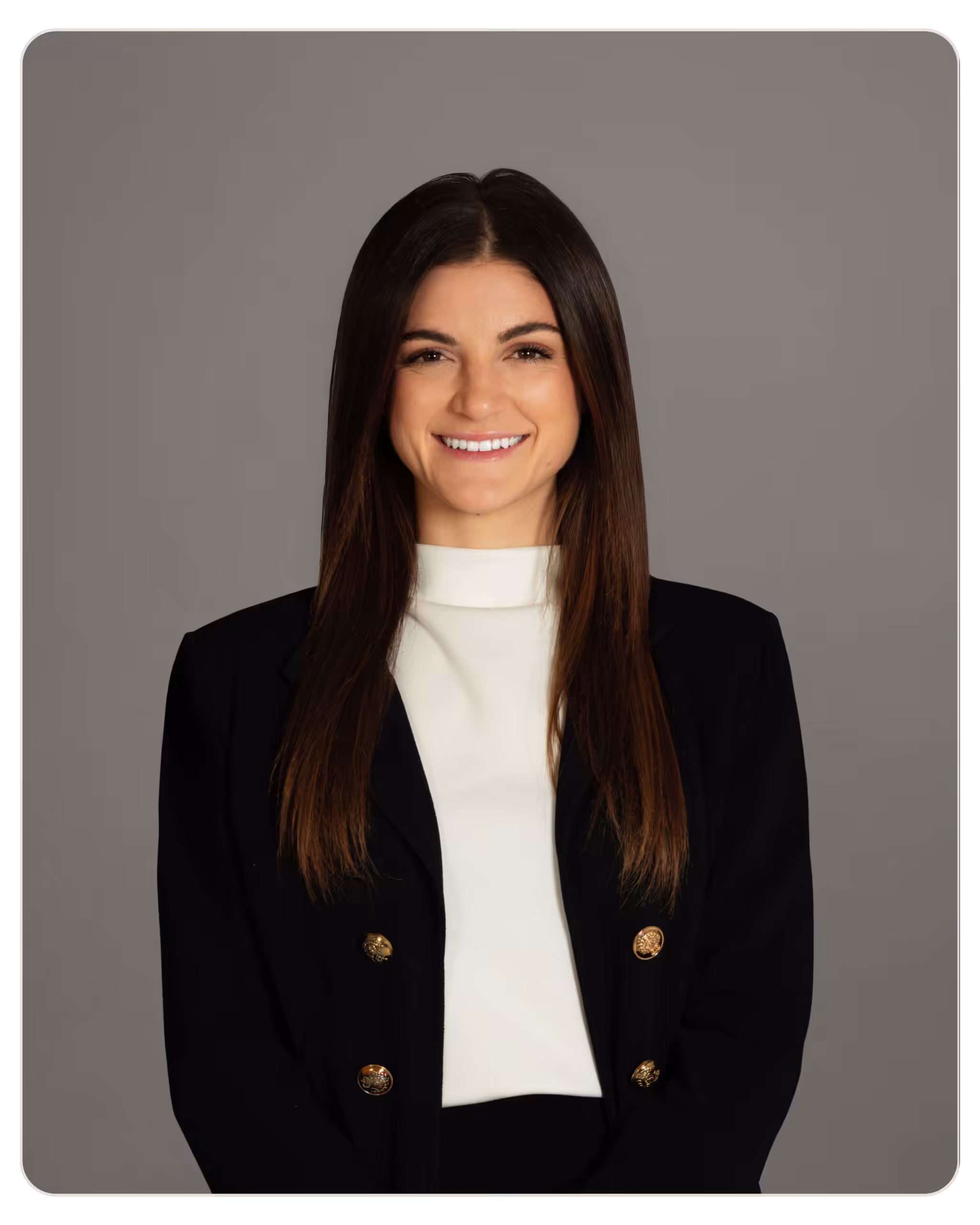 Kandela Samantha Necolettos Smiling woman with long dark hair in a black blazer and white blouse against a gray backdrop (professional portrait).