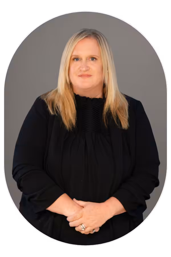 Professional portrait of a middle-aged woman with long blonde hair in a black blouse, against a gray studio backdrop.