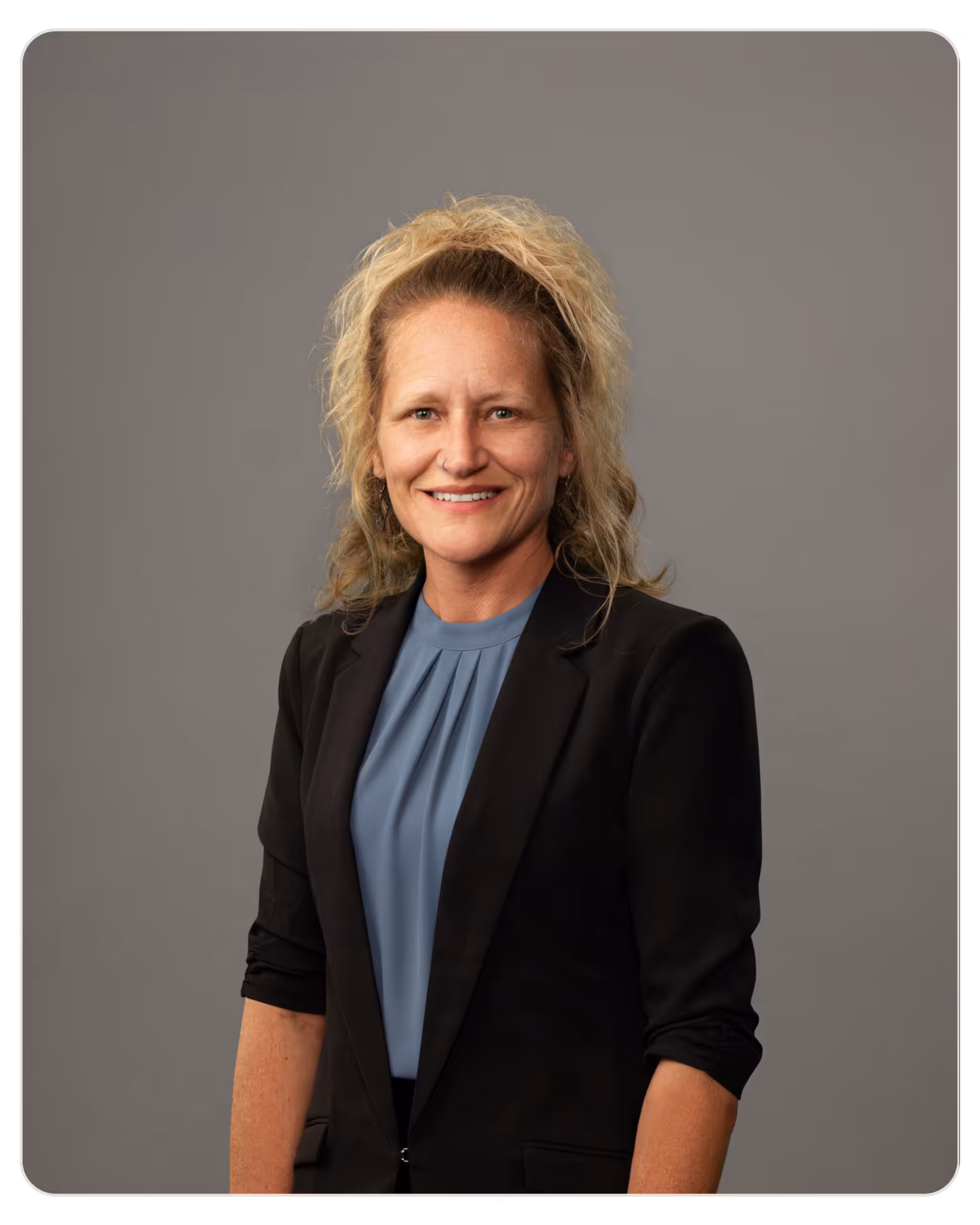 Skylight Dawn Griffith Portrait of a smiling blonde woman in a black blazer and blue blouse, posed for a professional head-and-shoulders portrait against a gray backdrop.