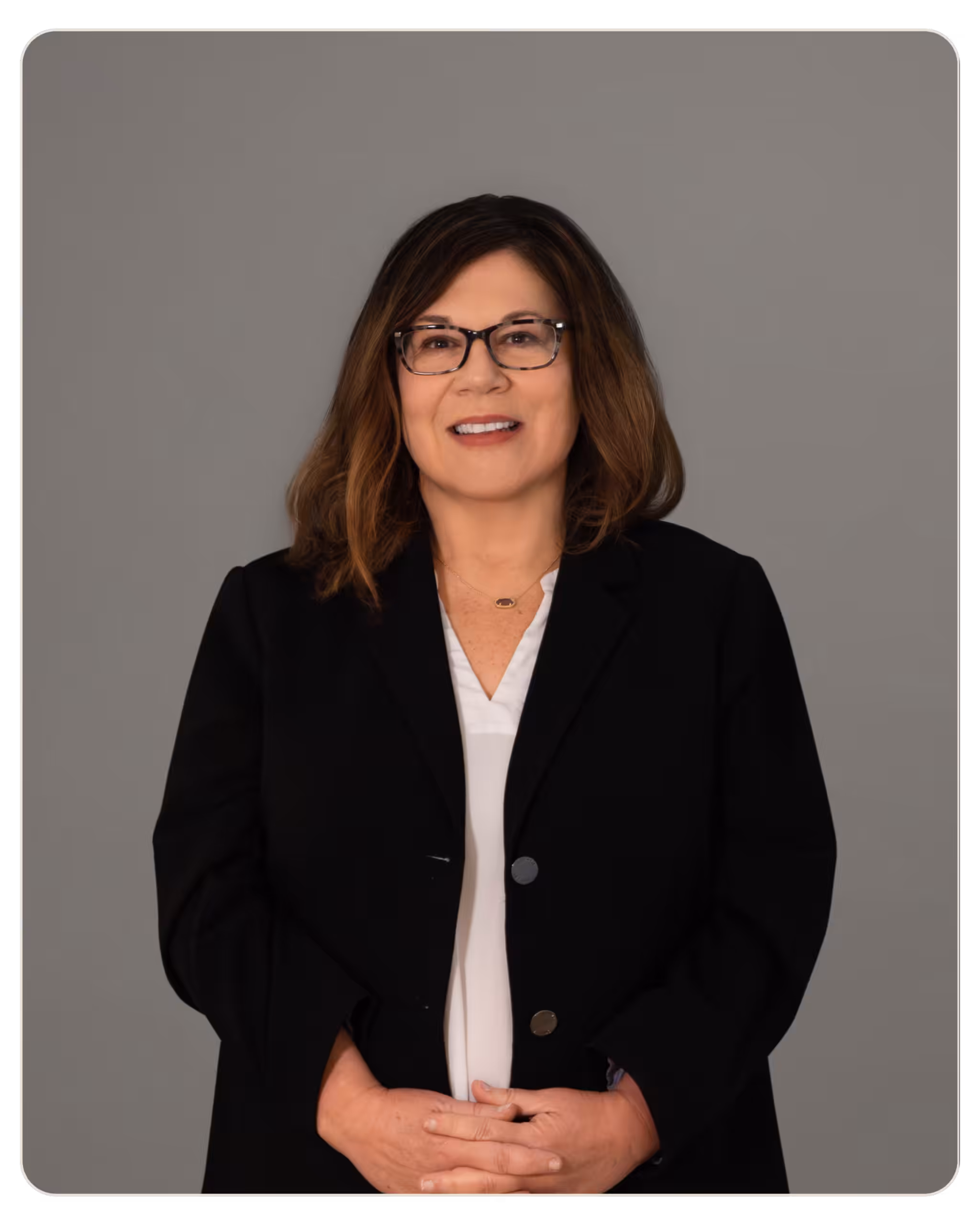 Kimberly McLaughlin, Program Supervisor at Skylight Recovery Center. Smiling professional headshot of a woman with glasses in a black blazer and white blouse against a gray backdrop, hands folded in front.