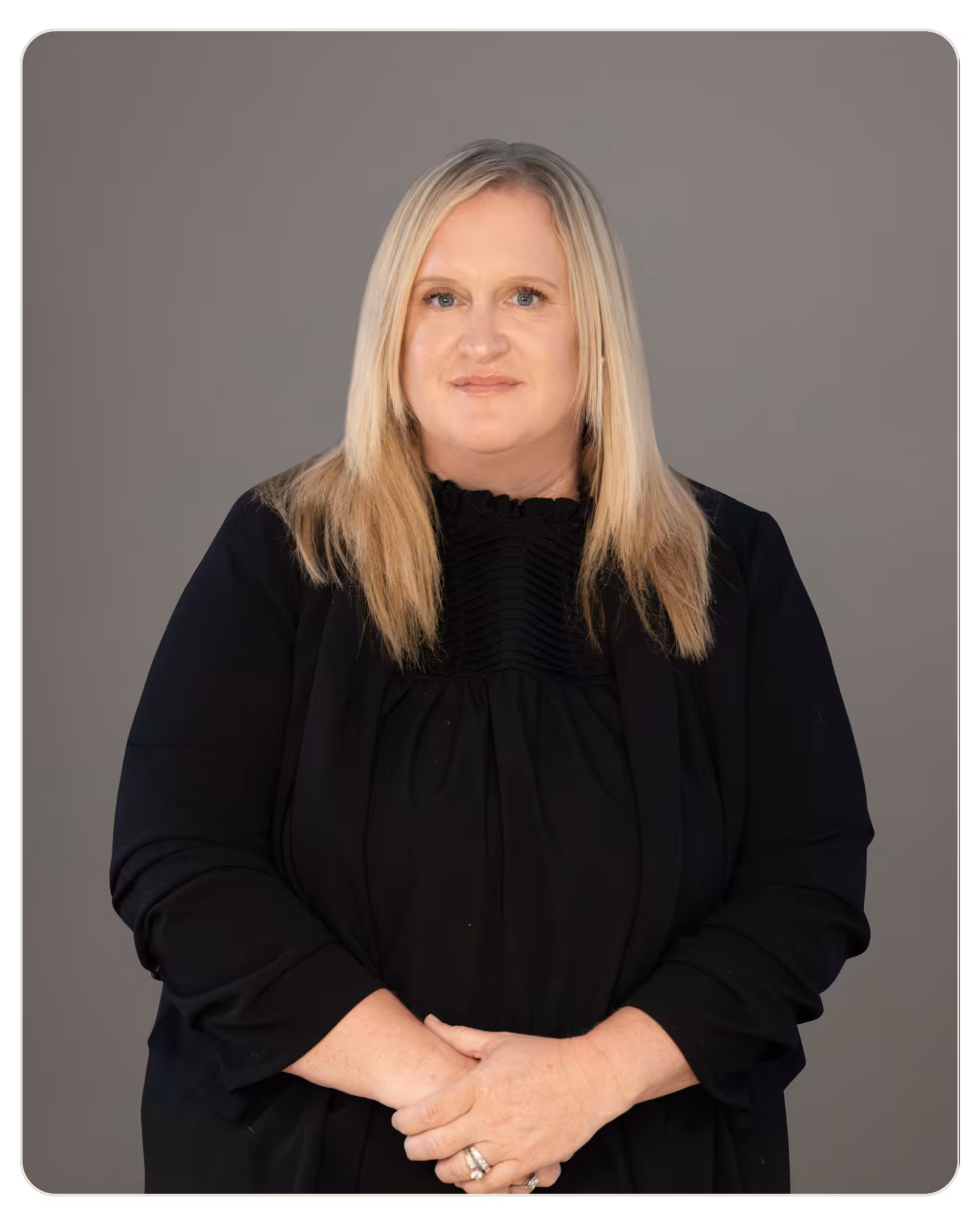 Professional portrait of a middle-aged woman with long blonde hair in a black blouse, against a gray studio backdrop. Portrait of a middle-aged woman with long blonde hair wearing a black blouse, standing with arms folded against a gray backdrop