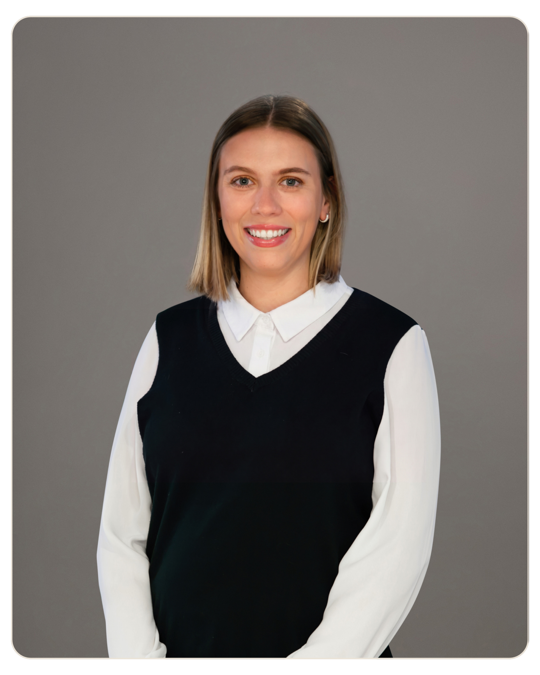 Smiling woman with shoulder-length blonde hair, white blouse under a black sweater vest, gray background edge-curved.