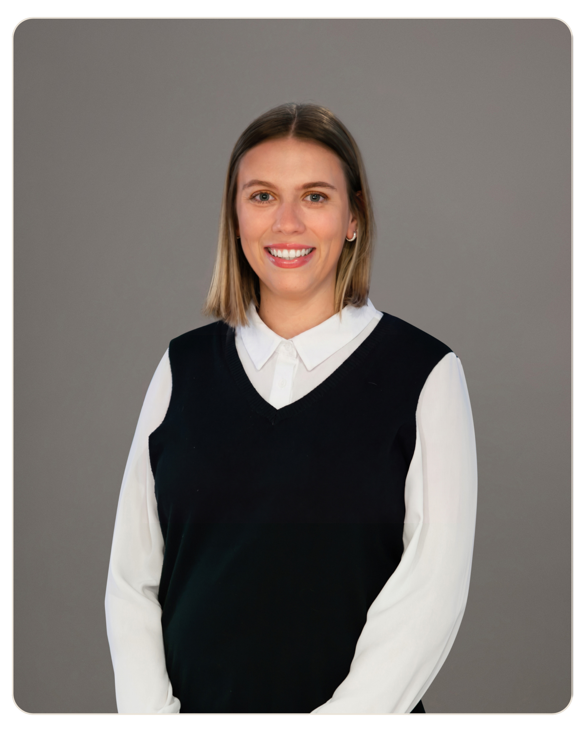 Smiling woman with shoulder-length blonde hair, white blouse under a black sweater vest, gray background edge-curved.