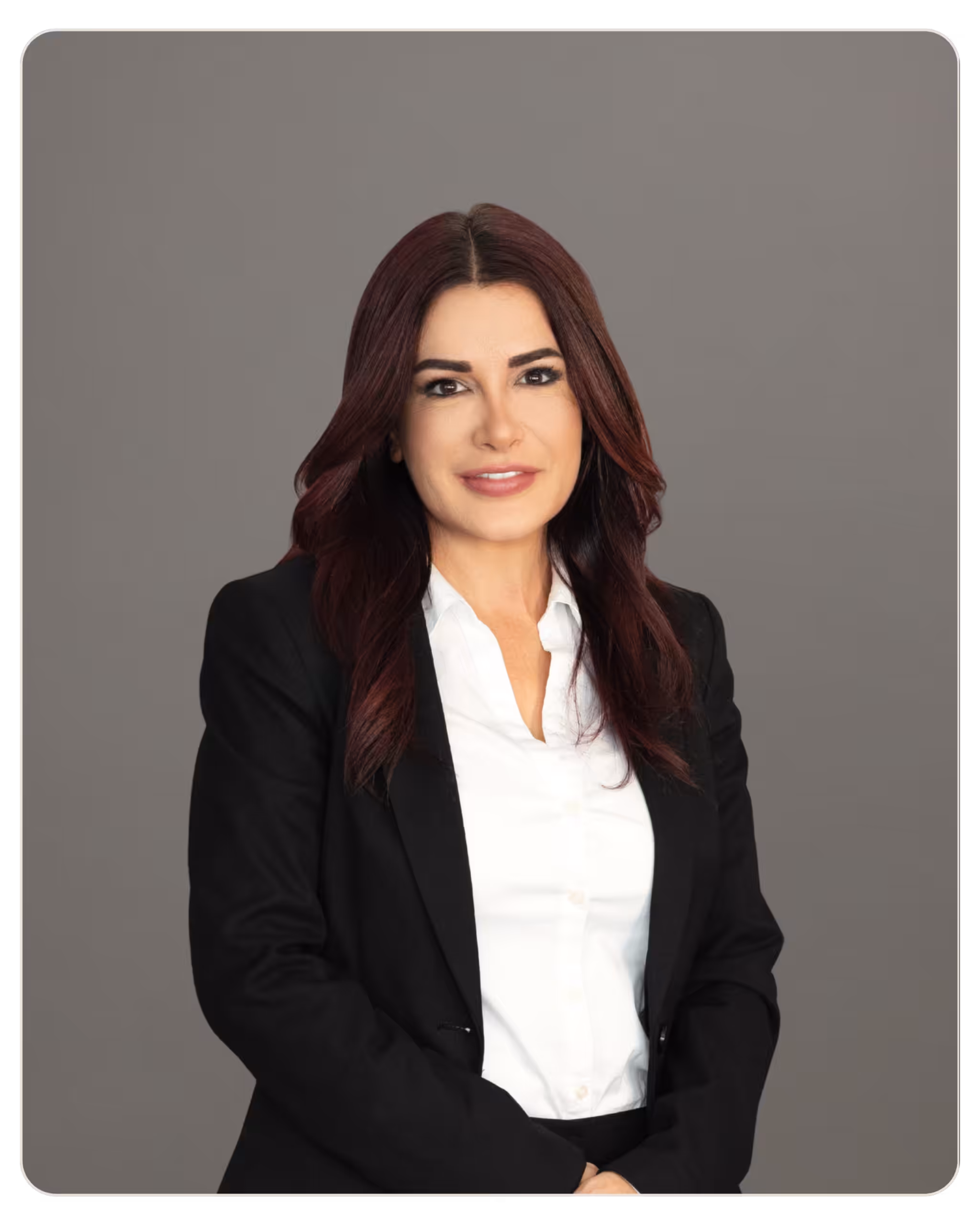Beacon Rochelly Giraud LMHC, LPCC, MCAP. Professional woman in a black blazer and white blouse, standing with arms crossed against a gray studio backdrop.