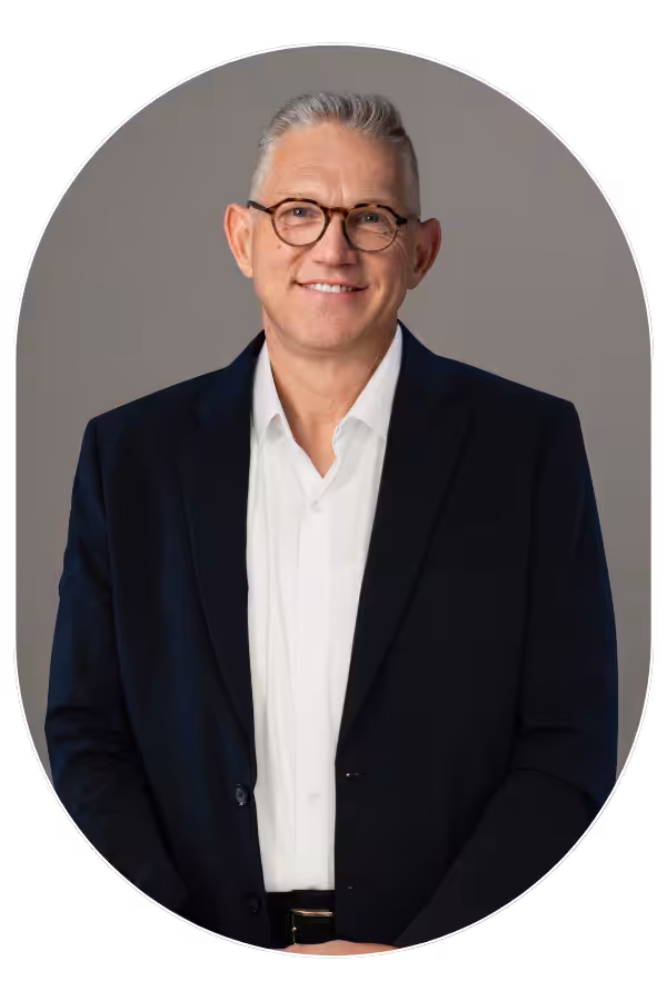 Portrait of a smiling middle-aged man in a dark suit and white shirt, wearing glasses.