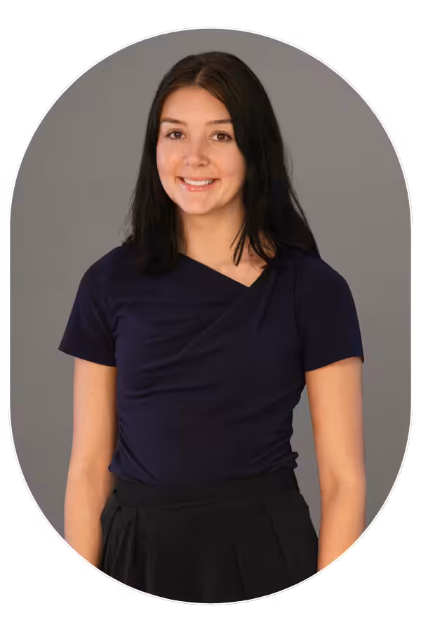 Smiling woman with shoulder-length dark hair in a navy top and black skirt, posed against a gray backdrop.