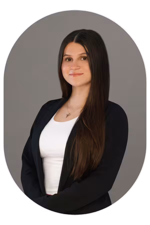 Professional portrait of a young woman with long dark hair, wearing a black blazer and white top, against a neutral gray background.
