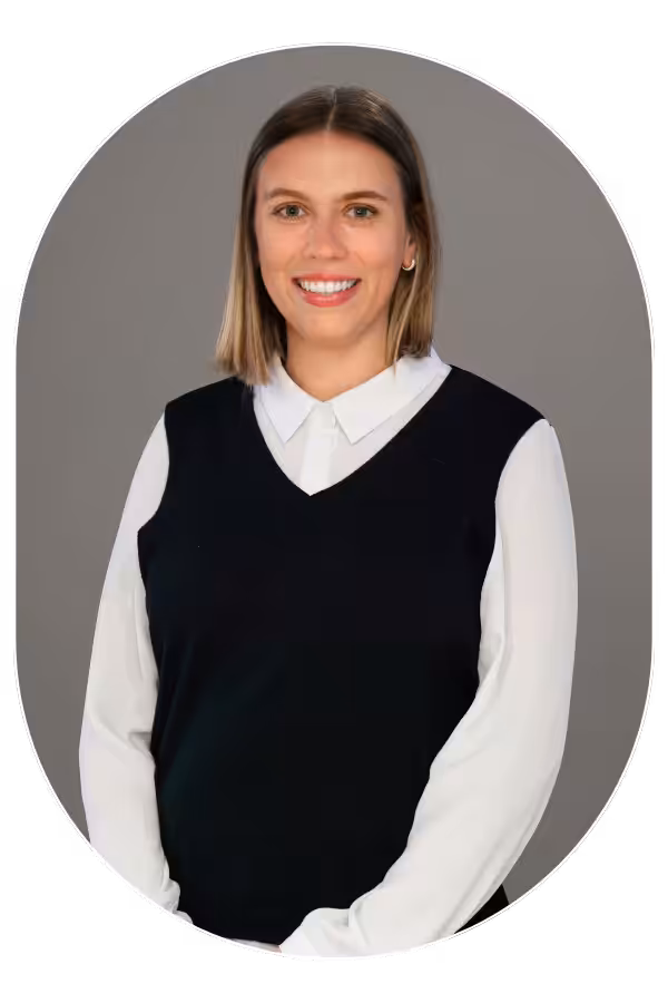 Smiling woman with shoulder-length blonde hair, white blouse under a black sweater vest, gray background edge-curved.