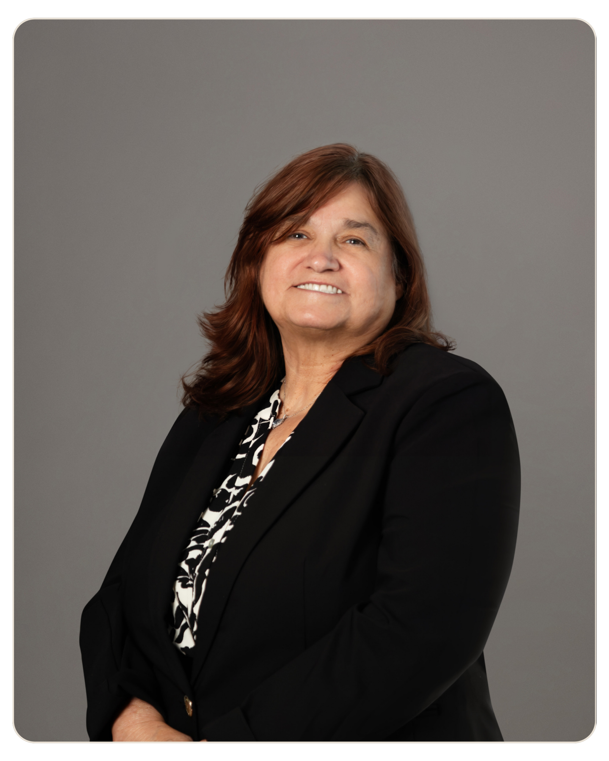 Toni Lopez, MS Primary Therapist Smiling woman in a white striped blouse stands against a gray backdrop.